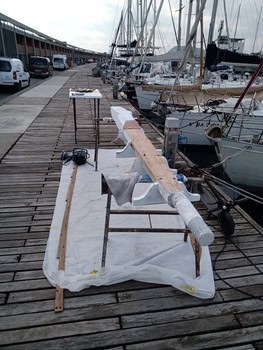 El mástil del Grandval Náutico reposa sobre caballetes, envuelto en plástico, en un muelle de madera junto a los barcos. Cerca de allí, las herramientas y el equipo esperan el mantenimiento práctico de los barcos en Barcelona, para garantizar que cada embarcación esté lista para su próxima aventura marítima.