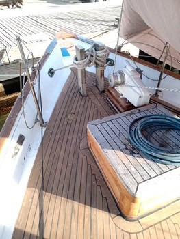 Cubierta de madera de un velero con cabos enrollados, un cabrestante y una manguera azul junto al muelle náutico de Grandval, perfecta para mantenimiento de barcos en Barcelona.