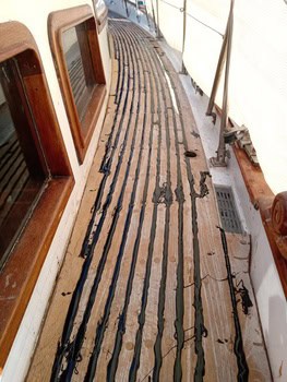 La cubierta de madera del barco, adornada con masilla negra, muestra signos de deterioro parcial. Los reflejos de las ventanas insinúan un día soleado, perfecto para una salida en Grandval náutico o para realizar algún mantenimiento de barcos en Barcelona.