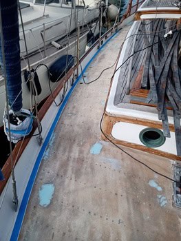 La cubierta de madera de un barco en proceso de reparación, con zonas lijadas y tablones de madera. Al fondo, las embarcaciones que lo rodean le dan a la escena el encanto náutico característico del reconocido servicio de mantenimiento de barcos en Barcelona de Grandval náutico.