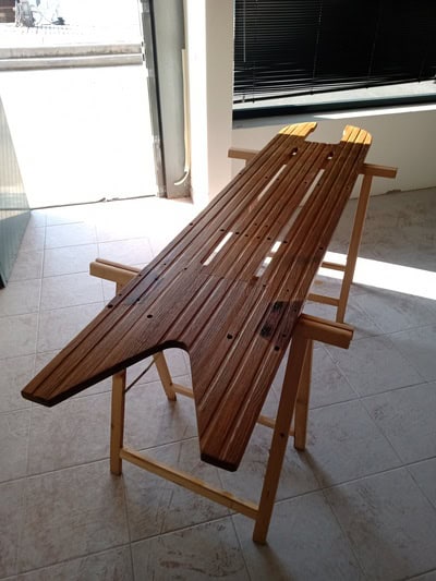 Una tabla de surf de madera en proceso de construcción reposa sobre un soporte en una sala bien iluminada de Grandval Náutico. La tabla presenta ranuras y un diseño en forma de cola de pez que recuerdan la artesanía que se ve en los tradicionales trabajos de mantenimiento de barcos en Barcelona.