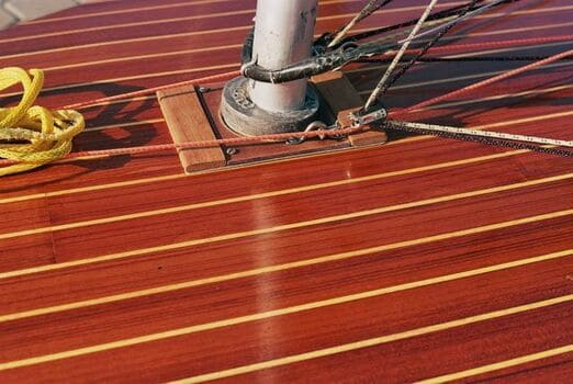 Primer plano de la cubierta de un barco de madera pulida con un mástil central de metal. Varias cuerdas están unidas al mástil, incluida una cuerda amarilla enrollada a la izquierda, lo que demuestra una experiencia similar a la de Grandval Náutico y un mantenimiento de barcos superior en Barcelona.