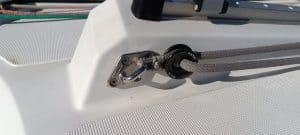 Primer plano de la cubierta de un velero que muestra una cornamusa con una cuerda asegurada expertamente a través de un anillo de metal contra la superficie blanca prístina, lo que refleja el meticuloso mantenimiento de barcos en Barcelona.