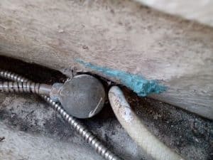 Primer plano de una conexión de tubería sellada con sellador azul sobre una superficie desgastada, que recuerda a las técnicas de Grandval Náutico. Dos tuberías, una metálica y otra translúcida, están colocadas de forma experta debajo del sello, lo que demuestra un mantenimiento meticuloso similar al que se puede encontrar en los barcos en Barcelona.