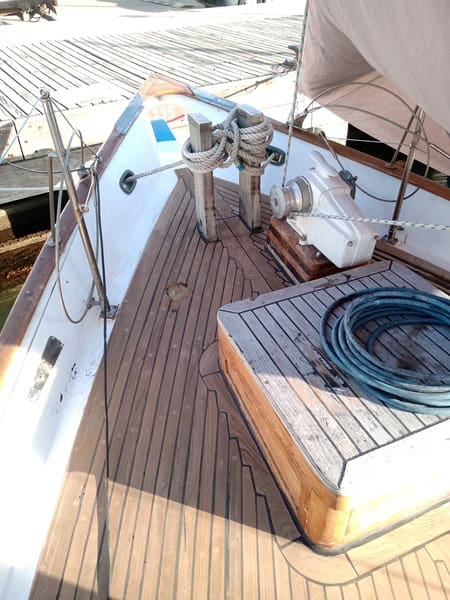 La cubierta de un barco muestra suelos de madera, cabos de amarre, una manguera enrollada y un cabrestante, lo que ejemplifica el meticuloso mantenimiento de barcos en Barcelona.