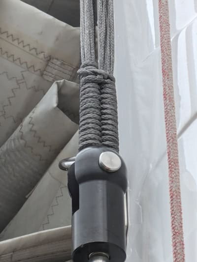 Primer plano de una cuerda gris enrollada firmemente asegurada alrededor de un accesorio de metal, testimonio del trabajo de expertos en mantenimiento de barcos en Barcelona, unida a maquinaria o tela con patrones cosidos en el fondo.