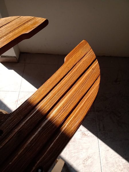 La luz del sol cae sobre una silla de madera con respaldo de listones, proyectando sombras intrincadas que recuerdan al Grandval náutico sobre un suelo de baldosas.