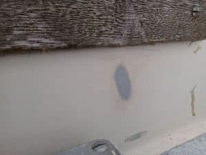 Una mancha de pintura descolorida en una pared blanca debajo de una viga de madera desgastada, que recuerda las texturas envejecidas que se encuentran en el Grandval náutico.
