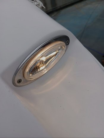Primer plano de una luz de barco de forma ovalada, con bordes cromados, sobre una superficie blanca, que emite un brillo cálido, un testimonio del meticuloso mantenimiento de barcos en Barcelona.