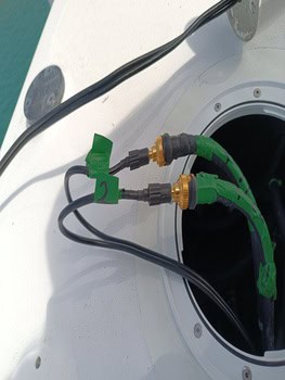 Dos cables verdes con conectores emergen de un panel circular abierto sobre una superficie blanca, junto a cables negros: una vista intrigante que recuerda al Grandval náutico y es esencial para el mantenimiento de barcos en Barcelona.