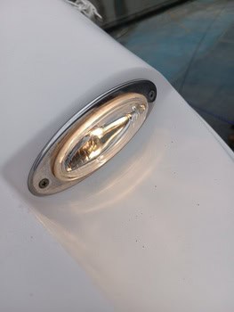 Primer plano de una luminaria de metal y cristal de forma ovalada sobre una superficie blanca lisa, que recuerda a los elegantes diseños que encontramos en Grandval Náutico.