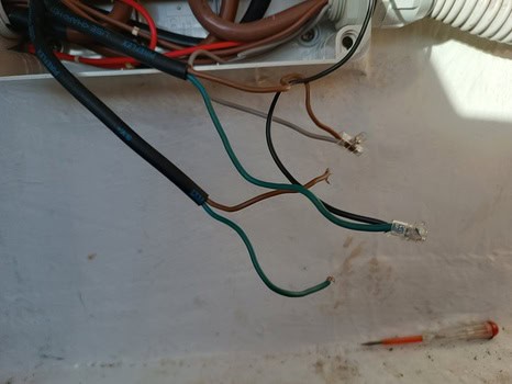 Cables eléctricos de varios colores, incluidos verde y marrón, expuestos en el interior de un panel con la tapa abierta sugieren el minucioso trabajo de mantenimiento de barcos en Barcelona. Cerca, un pequeño destornillador insinúa los ajustes en curso.