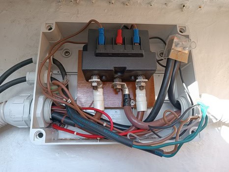 Dentro de esta caja de conexiones eléctricas, múltiples cables y conectores de colores están dispuestos de forma intrincada sobre un soporte de madera, reflejando la meticulosa artesanía que se observa en Grandval Náutico.
