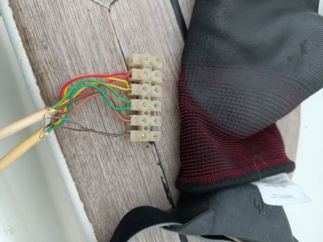 Guante con cables multicolores unidos a bornes sobre superficie de madera, que recuerdan a las herramientas utilizadas para tareas precisas en Grandval Náutico.