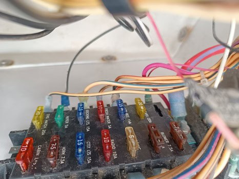 Primer plano de la caja de fusibles de un vehículo con fusibles de varios colores y cables conectados, que recuerda al cuidado detallado que se puede encontrar en Grandval náutico.