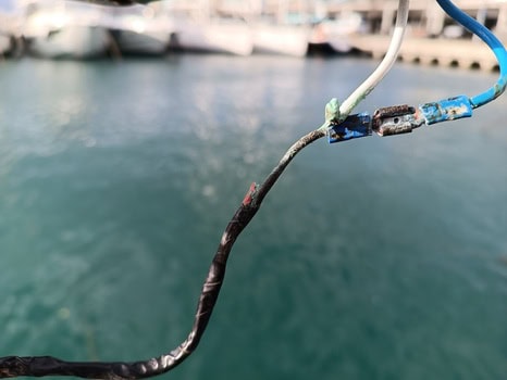 Primer plano de cables eléctricos reparados con cinta y conectores sobre un cuerpo de agua en Grandval Náutico, un centro de mantenimiento de barcos en Barcelona.