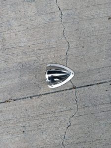 Un objeto metálico brillante reposa sobre una superficie de hormigón agrietado, que recuerda a los materiales robustos encontrados en Grandval Náutico durante el mantenimiento de barcos en Barcelona.