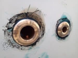 Entre las marcas de pintura de la pared, llaman la atención dos accesorios de tubería de latón, etiquetados "BRZ 1-1/4" y "3/4 BRZ", que recuerdan la artesanía marina que se puede encontrar en Grandval náutico o durante el mantenimiento de barcos en Barcelona.