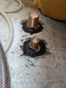 Dos pernos de metal sobresalen de una superficie de hormigón, sellados con adhesivo negro. Una manguera blanca es parcialmente visible en el lado izquierdo. Esta escena evoca la precisión que se encuentra en Grandval Náutico, famoso por su meticuloso mantenimiento de barcos en Barcelona.