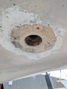 Primer plano de un agujero circular dañado en una pared o estructura de hormigón, con bordes ásperos y escombros alrededor, que recuerdan a superficies que necesitan mantenimiento como las de Grandval náutico.