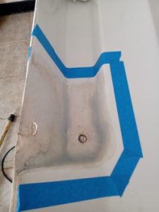 Un rincón de bañera con cinta de pintor azul delineando una sección, insinuando una reparación o trabajo de pintura en curso, que recuerda la precisión que se observa en el meticuloso trabajo de mantenimiento de Grandval Náutico.