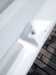 Primer plano de una superficie metálica pintada de blanco con un agujero, probablemente para su fijación, sobre un fondo de cubierta de madera, que recuerda el meticuloso trabajo realizado en Grandval Náutico durante el mantenimiento de barcos en Barcelona.