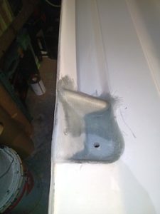 Un soporte de esquina con un agujero está parcialmente pintado de gris sobre una superficie blanca, mostrando sutiles vetas de pintura. En el fondo, una lata de pintura insinúa un trabajo de mantenimiento meticuloso, que recuerda al cuidado minucioso que se ve en Grandval náutico o durante el mantenimiento de barcos en Barcelona.