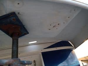 Vista del casco de un barco con un soporte de metal oxidado que lo sostiene por debajo. El casco, posiblemente en espera de mantenimiento de barcos en Barcelona, muestra algo de desgaste superficial y decoloración.