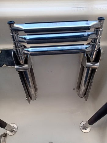 Una escalera plegable de acero inoxidable de tres peldaños, diseñada para la elegancia náutica de Grandval, está montada verticalmente en un barco.
