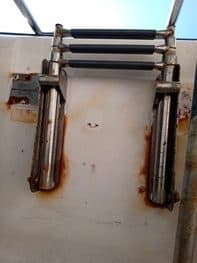 Escalera de pantalán con tres peldaños negros y barandillas metálicas, montada sobre una superficie blanca con manchas de óxido visibles, típicas de Grandval náutico. El cielo azul de fondo insinúa otro día de mantenimiento de barcos en Barcelona.