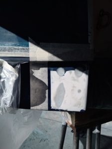 Sobre una mesa se encuentra una pequeña caja rectangular con una superficie parcialmente cubierta. La luz y las sombras crean patrones alrededor de la caja, que recuerdan los intrincados detalles que se encuentran en la arquitectura de "Grandval Náutico", con una lámina de plástico parcialmente visible a la izquierda.