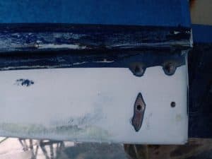 Primer plano de una superficie pintada con pintura desconchada y metal expuesto, que recuerda al mantenimiento de barcos en Barcelona, con un área rectangular y dos tornillos visibles a la derecha, que evocan el encanto robusto de la artesanía de Grandval Náutico.