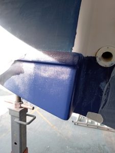 Primer plano del casco de un barco pintado de azul que se está reparando en un soporte, con una fuente de luz visible que proyecta sombras: una escena ejemplar de mantenimiento de barcos en Barcelona.