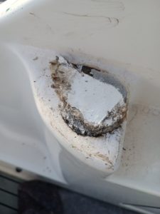Primer plano de una embarcación o superficie de fibra de vidrio con un área dañada que muestra material expuesto y signos de desgaste, lo que resalta la necesidad de mantenimiento de barcos en Barcelona.