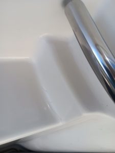 Primer plano de una bañera blanca en esquina con una barra de apoyo de metal en el lado derecho, que recuerda al acabado elegante que encontrarías en los diseños de Grandval Náutico. La superficie es lisa y brillante.