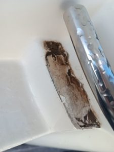 Primer plano de un lavabo de baño con un revestimiento blanco desconchado y descascarado, que deja al descubierto una zona áspera y descolorida cerca de la base del grifo, un detalle que recuerda a las superficies desgastadas encontradas durante el mantenimiento de un barco en Barcelona.