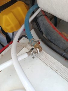 Dentro del espacio mecánico, las mangueras azules y blancas están conectadas expertamente con una válvula de latón y abrazaderas de metal, asemejando la precisión que esperarías de Grandval Náutico, conocido por su impecable mantenimiento de barcos en Barcelona.