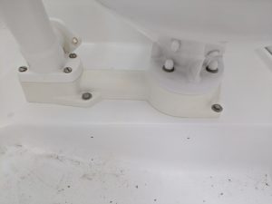 Vista de cerca de un componente mecánico o de fontanería de color blanco con tornillos y soportes, montado sobre una superficie blanca texturizada, que recuerda la precisión que encontramos en el experto mantenimiento de barcos en Barcelona de Grandval Náutico.