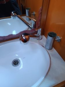Lavabo con grifería y dosificador de jabón metálico sobre encimera, que evoca la elegancia de Grandval Náutico. Un espejo con marco de madera se sitúa sobre el lavabo, completando esta tranquilidad de inspiración náutica.