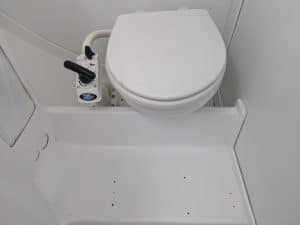 Baño compacto equipado con inodoro marino blanco con bomba manual, perfecto para los amantes de Grandval Náutico y para garantizar un mantenimiento de barcos en Barcelona de primer nivel.