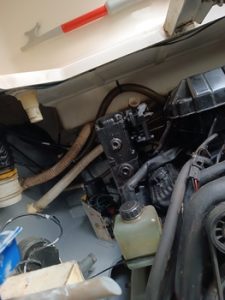 Vista interior del compartimento del motor de un barco que muestra mangueras, un recipiente de plástico y varios componentes mecánicos. Un bichero con asa roja se encuentra en la parte superior. Perfecto para aquellos interesados en Grandval náutico o que buscan un experto en mantenimiento de barcos en Barcelona.