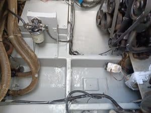 Compartimento del motor con mangueras, cables y componentes mecánicos visibles. Hay un filtro de combustible y poleas. Superficies pintadas de gris cubren el área, lo que recuerda la meticulosa atención al detalle de Grandval náutico en su mantenimiento de barcos en Barcelona.