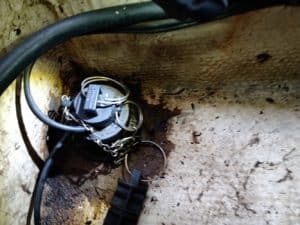 Primer plano de un objeto negro, que recuerda al encanto náutico de Grandval, asegurado con una cadena de metal en el interior de un contenedor desgastado y oxidado.